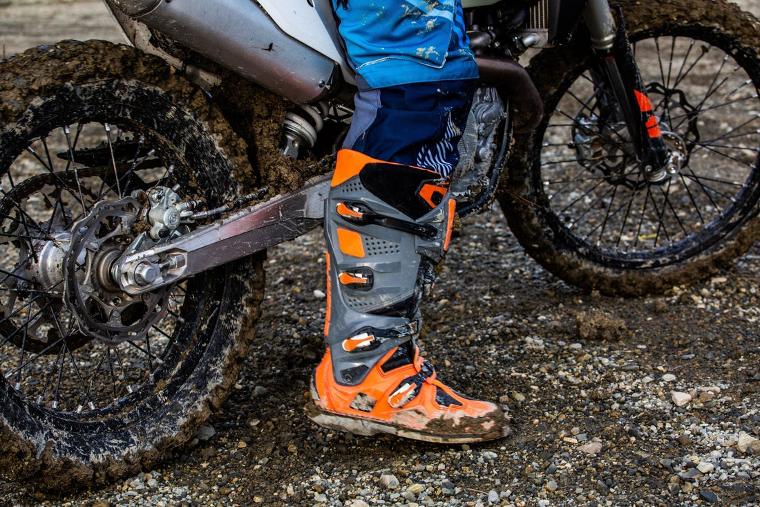 Orange motocross boots on a muddy dirt bike with feet planted on the floor